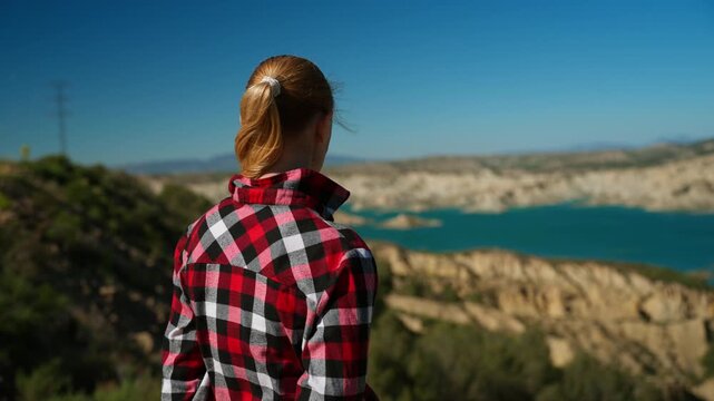 Confident mature woman stand on cliff overlook turquoise lake and dramatic canyon landscape. Freedom, self-discovery, wellbeing and embracing life journey concept in nature.