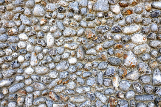 An old rustic stone wall with a pattern of round Norfolk flint stone pebbles in closeup
