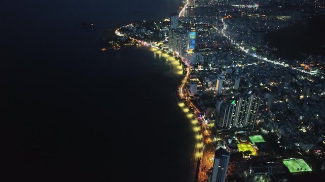 Night aerial panorama of Nha Trang Bay with glowing coastal boulevard and extensive urban skyline.