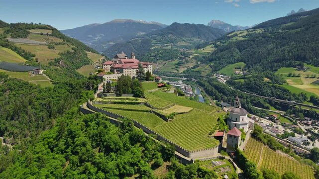Aerial view of Monastero di Sabiona on steep cliff with vineyards, scenic fortress in South Tyrol mountains of Italy. Historic Sabiona monastery looking over Eisack valley