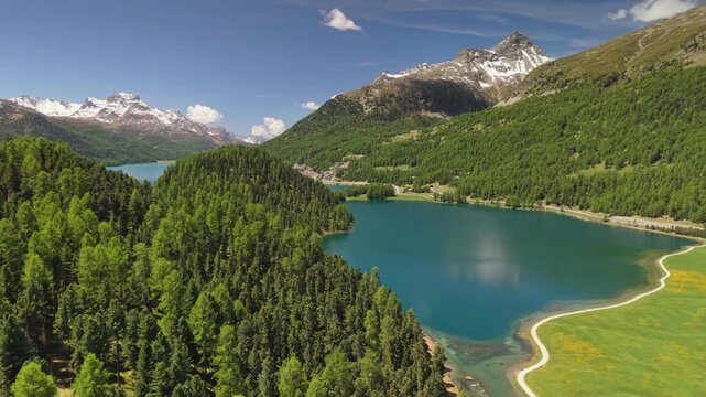 Stunning aerial view of turquoise Lake Champfer near Sankt Moritz, dense green pine forests and snow mountains in Switzerland. Champfer lake with footpaths on shore, Engadin valley of Swiss Alps