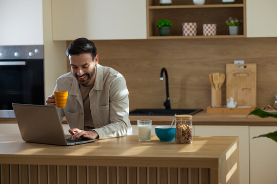 Man sips coffee working on laptop at home