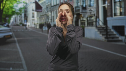 Fototapeta premium Woman cupping hands around mouth shouting to call attention on a city street with row houses and parked car; urgency warning.