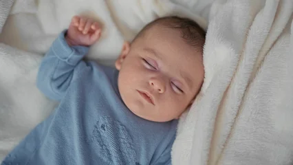 Baby sleeping on plush blanket with arm raised and fist gently clenched in studio  serenity comfort bonding. © Krakenimages.com