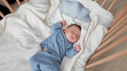 Baby sleeping with clenched fists and one hand near face on a soft blanket in a wooden crib inside a building  peaceful rest. © Krakenimages.com