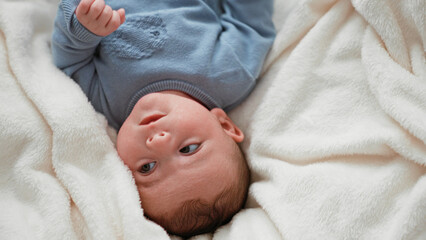Newborn boy lying on plush white blanket on bed, knit onesie, head turned with gentle gaze and tiny fists visible in studio  innocence calm. © Krakenimages.com