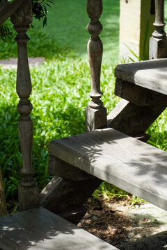 Rustic wooden staircase with ornate balusters in a lush green garden setting
