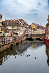 Obraz premium Early calm on Colmar canal with soft light, empty walkway and mirrored facades, ducks gliding through still water adding peaceful travel