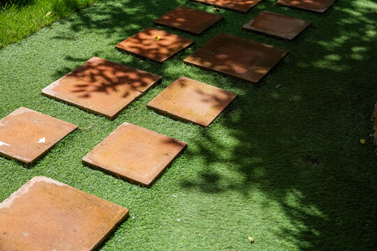 Terracotta stepping stones create a path across a vibrant green artificial lawn