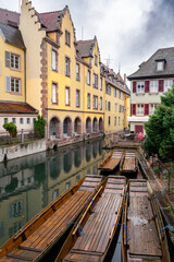 Fototapeta premium Row of wooden punts moored along narrow canal, yellow gabled facade providing colorful backdrop, rustic planks and oars suggesting gentle