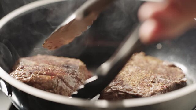 Seared beef fillets sizzling in a frying pan with tongs lifting one piece