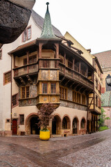 Ornate carved balcony and timbered bays overlooking damp square, detailed woodwork, stone arches, potted plants and quiet market feel © Oksana