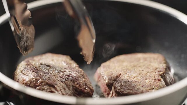 Close-up of two seasoned beef fillets searing in a dark frying pan