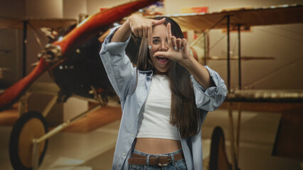 Woman framing a rectangle with her fingers and smiling at an airplane propeller inside a museum building  playful curiosity. © Krakenimages.com