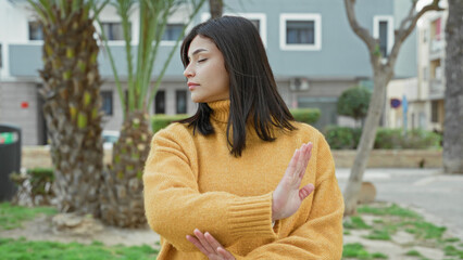 Fototapeta premium Woman shows palm forward stop gesture on street wearing yellow turtleneck sweater; boundary assertiveness determination.