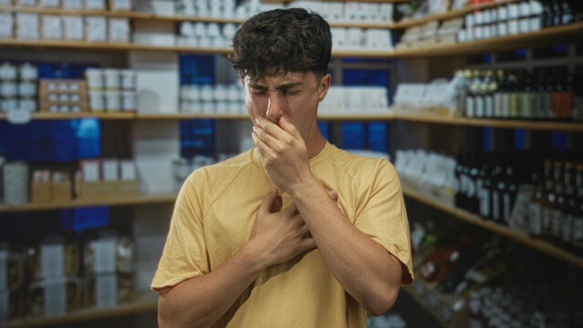 Young hispanic man covers mouth with hand and clutches chest while grimacing in a pharmacy building; nausea symptom.
