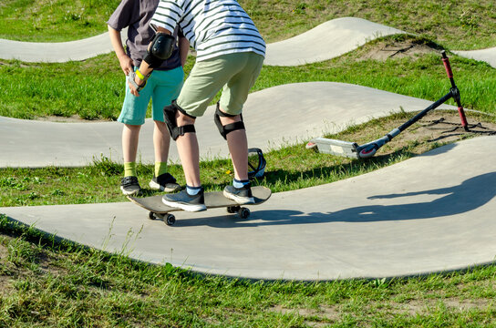 teen rides skateboard on concrete pump track while friend watches. learning to ride skateboard builds skills. this skateboard offers outdoor recreation and friendship for youth today.