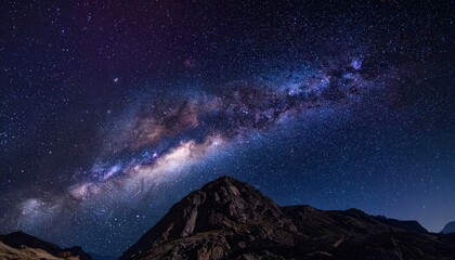 Fototapeta premium The Milky Way arches majestically over a rugged mountain peak under a sky full of stars.