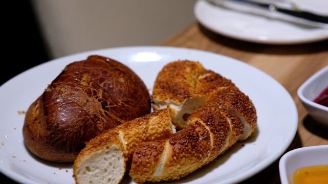 Pogaca and simit slices are served on a white plate as part of a breakfast table. Close-up scene showing Turkish breakfast presentation, bakery products and traditional savory pastry detail.