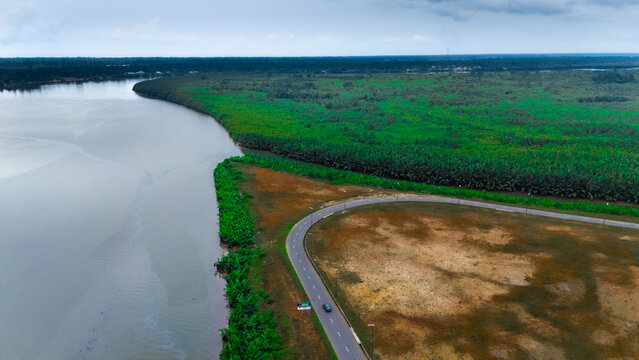 Aerial view of a winding road following the curve of a river, bordered by lush green vegetation and an open field in Minima, Rivers, Nigeria.