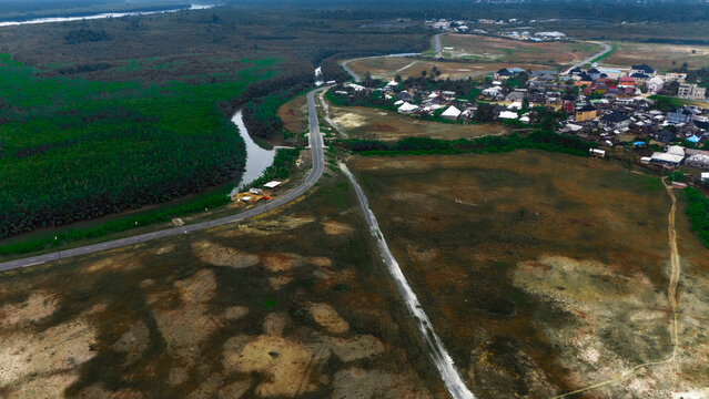 Aerial view of a winding road passing through rural landscape with a river and a small settlement in Rivers, Nigeria.