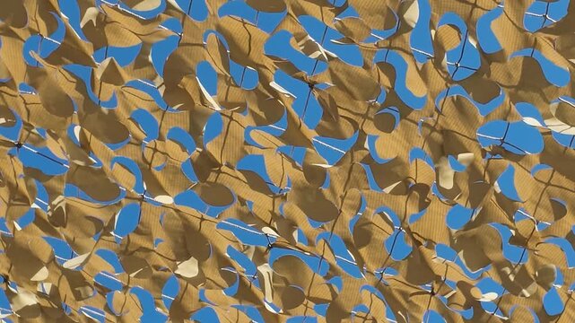 Alccudia Mallorca Spain. 01.06.2026. A close-up view of camouflage netting stretched taut, allowing sunlight to filter through its irregular pattern onto a bright blue sky