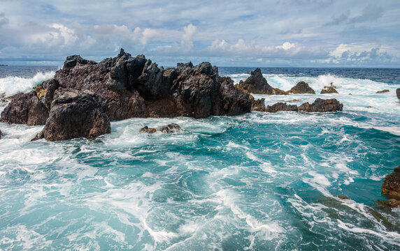 Powerful white ocean waves foaming and crashing into dark volcanic rock reefs near Porto Moniz natural pools, Madeira, Portugal.