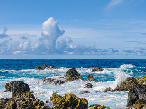 Powerful white ocean waves foaming and crashing into dark volcanic rock reefs near Porto Moniz natural pools, Madeira, Portugal.