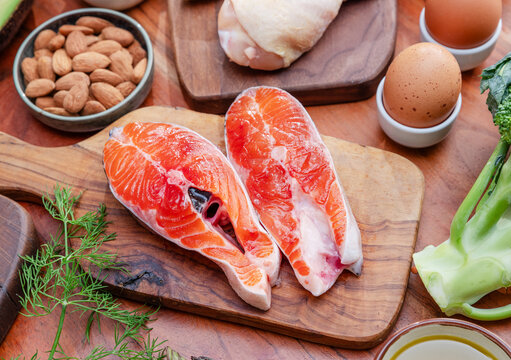 Two fresh raw salmon steaks with assortment of different food on a wooden board.