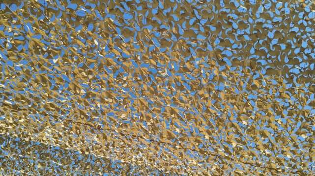 Alccudia Mallorca Spain. 01.06.2026. A close-up view of camouflage netting stretched taut, allowing sunlight to filter through its irregular pattern onto a bright blue sky