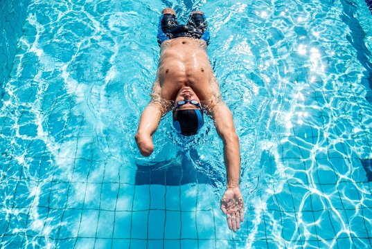A male paraswimmer with a missing arm competes in the backstroke in a bright blue swimming pool.