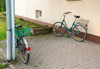 Two classic utility bicycles with baskets parked next to a residential building wall. The composition illustrates sustainable transportation, everyday cycling and urban neighborhood life. © Volha