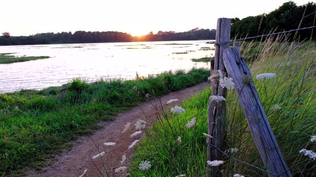 Static 4K shot from a walking path along the Auray River, Brittany, France, at high tide during a golden sunset. Wooden fence in the foreground.