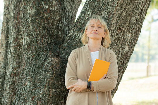 Dream and hope concept, old woman holding book and relax with close eye to think and dreaming under tree in park