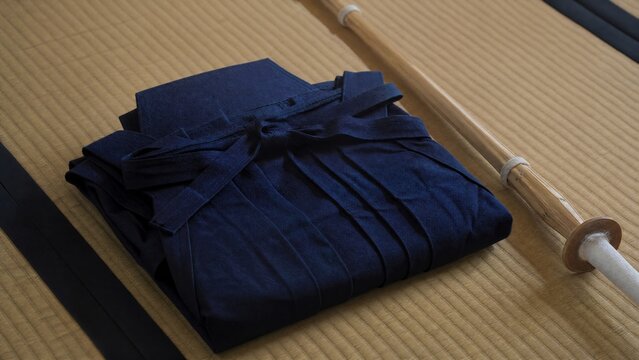 A neatly folded deep blue hakama and bamboo sword on tatami mat flooring. 