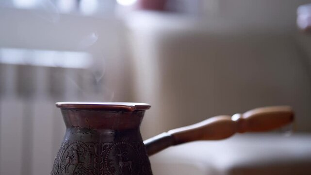 A close-up shot of hot, aromatic coffee steaming in a traditional copper cezve, with intricate patterns. The rising steam creates a cozy and inviting morning atmosphere. Slow motion.