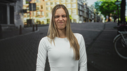 Fototapeta premium Young hispanic woman grimaces with scrunched nose and pursed lips on a street, standing center frame; annoyance.