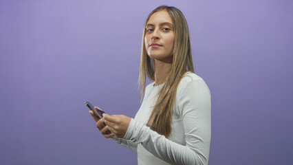 Naklejka premium Woman holding smartphone, texting with both hands, side profile against purple studio backdrop; contemplation focus.