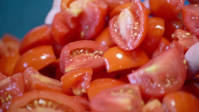 Female hands gently mix a pile of juicy chopped tomatoes against a blue background. This close-up shot captures the freshness of ingredients prepared for a healthy salad.