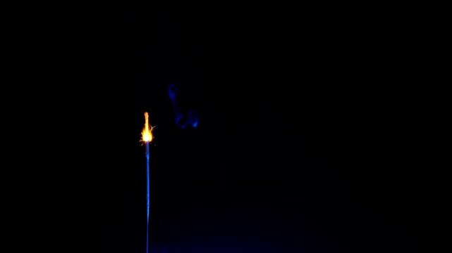 A single golden sparkler burns intensely emitting bright sparks against a pitch black background. Concept of celebration, holiday magic, festive atmosphere, and joyous occasions.