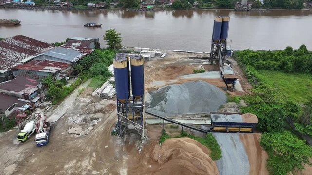 A view from above of a concrete plant on the riverbank in West Borneo, Indonesia, featuring silos, piles of gravel, and a conveyor system