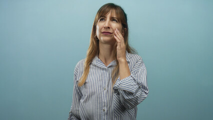 Woman touching cheek with hand in light blue studio wearing striped shirt and hoop earring  pensive reflection. © Krakenimages.com