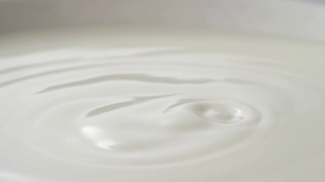 Slow motion close up of milk pouring and rippling into white bowl on tabletop in studio kitchen