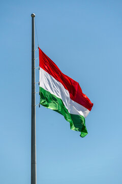 Hungarian flag waving on a flagpole against a clear blue sky during a sunny day