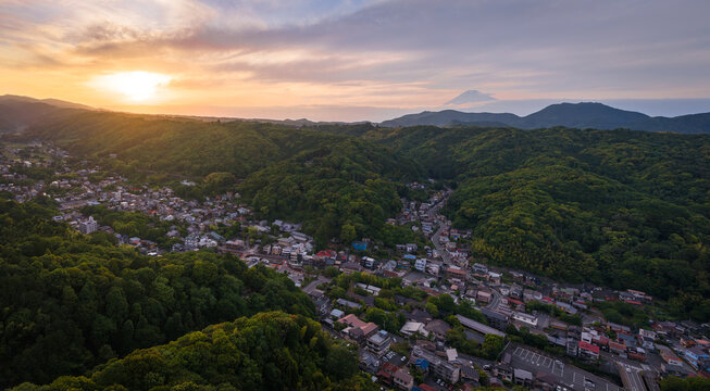 Aerial view of the historic town of Shuzenji nestled among lush green mountains at sunset with Mount Fuji visible in the distance in Izu, Shizuoka, Japan.