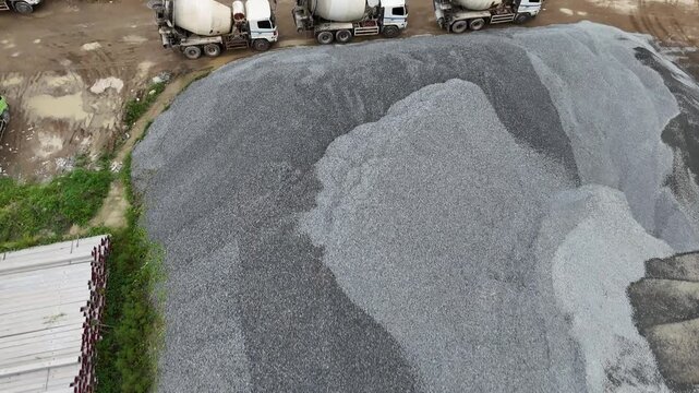 A view from above of piles of gravel and aggregate at a construction project storage site, along with cement trucks