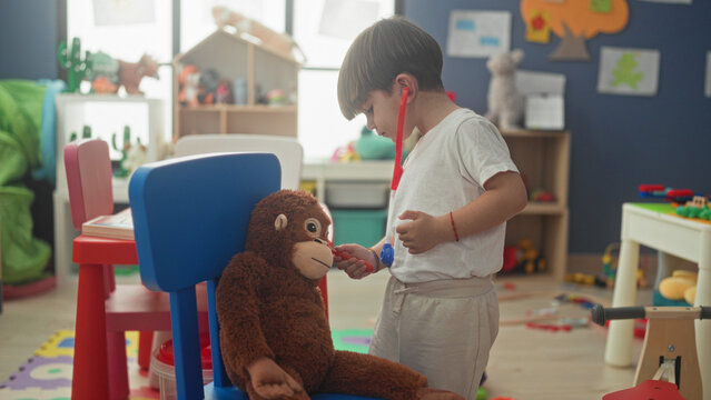 Boy holds red toy stethoscope to plush monkey and lifts earpieces to his ears while standing in a playroom building; playful curiosity.