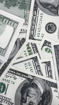 People handle and count many hundred dollar bills on a flat surface inside a room as light comes in during the afternoon.