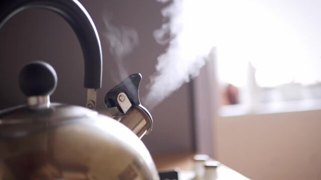 A stainless steel whistling kettle boils water on a kitchen stove while thick white steam rises from the spout. Concept of morning routine, tea preparation, and domestic comfort.