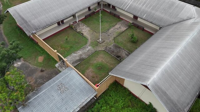 A view from the top of a simple, minimalist-style school building with a U-shaped layout surrounding a grassy courtyard and a flagpole.